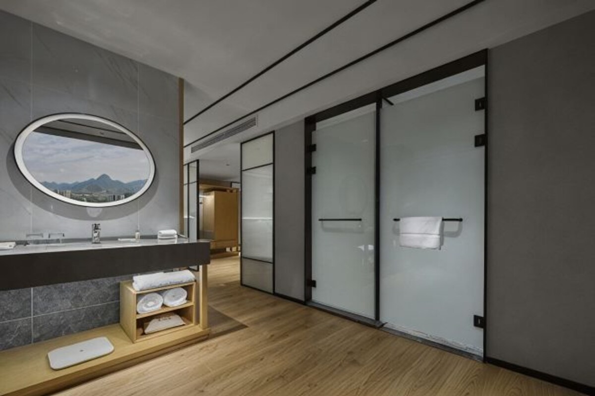 Un baño moderno con tocador de madera, un espejo redondo y vistas a la montaña.