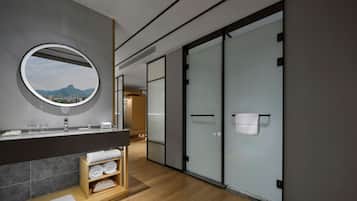 A modern bathroom with a large mirror, a wooden vanity, and a view of mountains through the window.