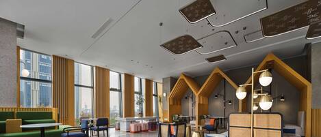 A modern interior with large windows, green seating, and a mix of round and rectangular tables.