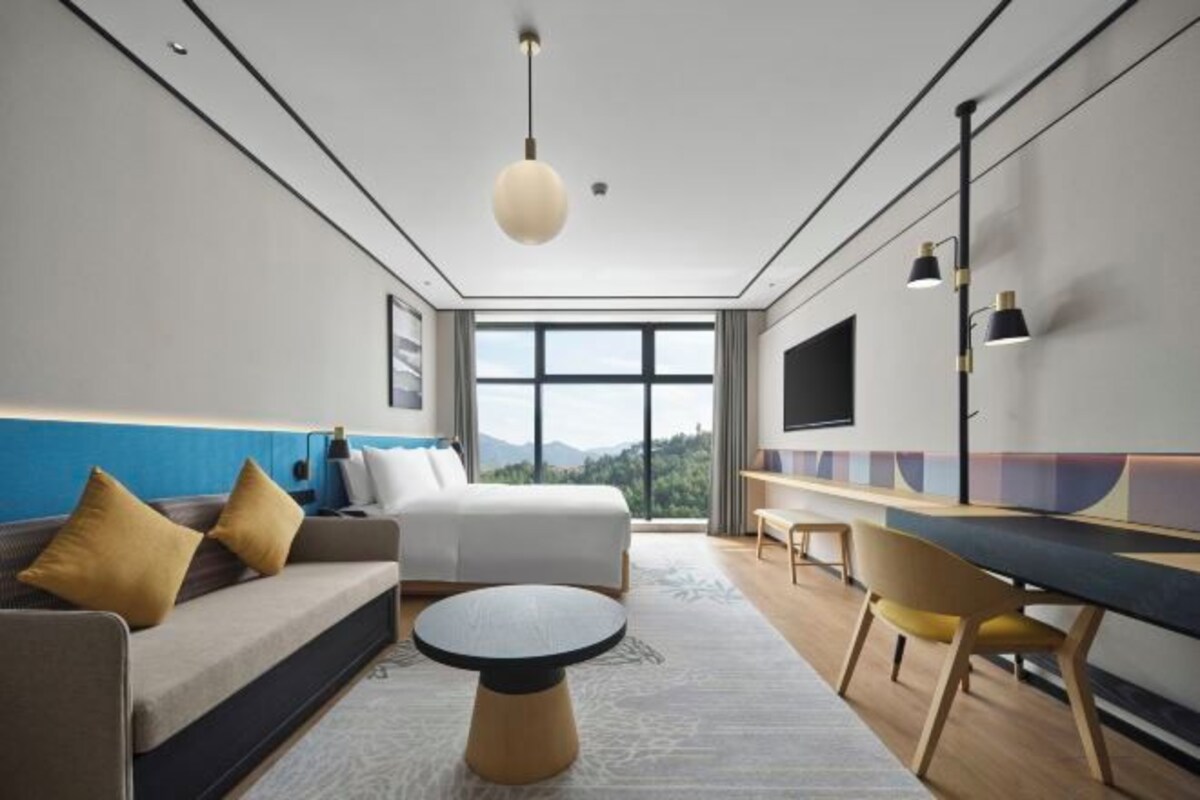 Una habitación de hotel moderna con una cama grande, un sofá, un escritorio y vistas al exterior.