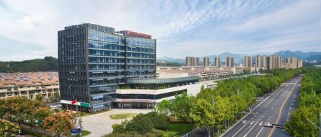 Un hotel moderno con fachada de vidrio, un patio ajardinado y vistas de edificios y montañas circundantes.