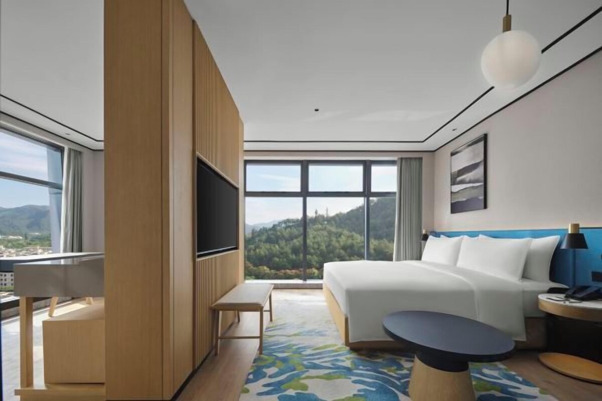 Ein modernes Hotelzimmer mit einem großen Bett, einem Fernseher, einem Schreibtisch und Blick auf die Berge.