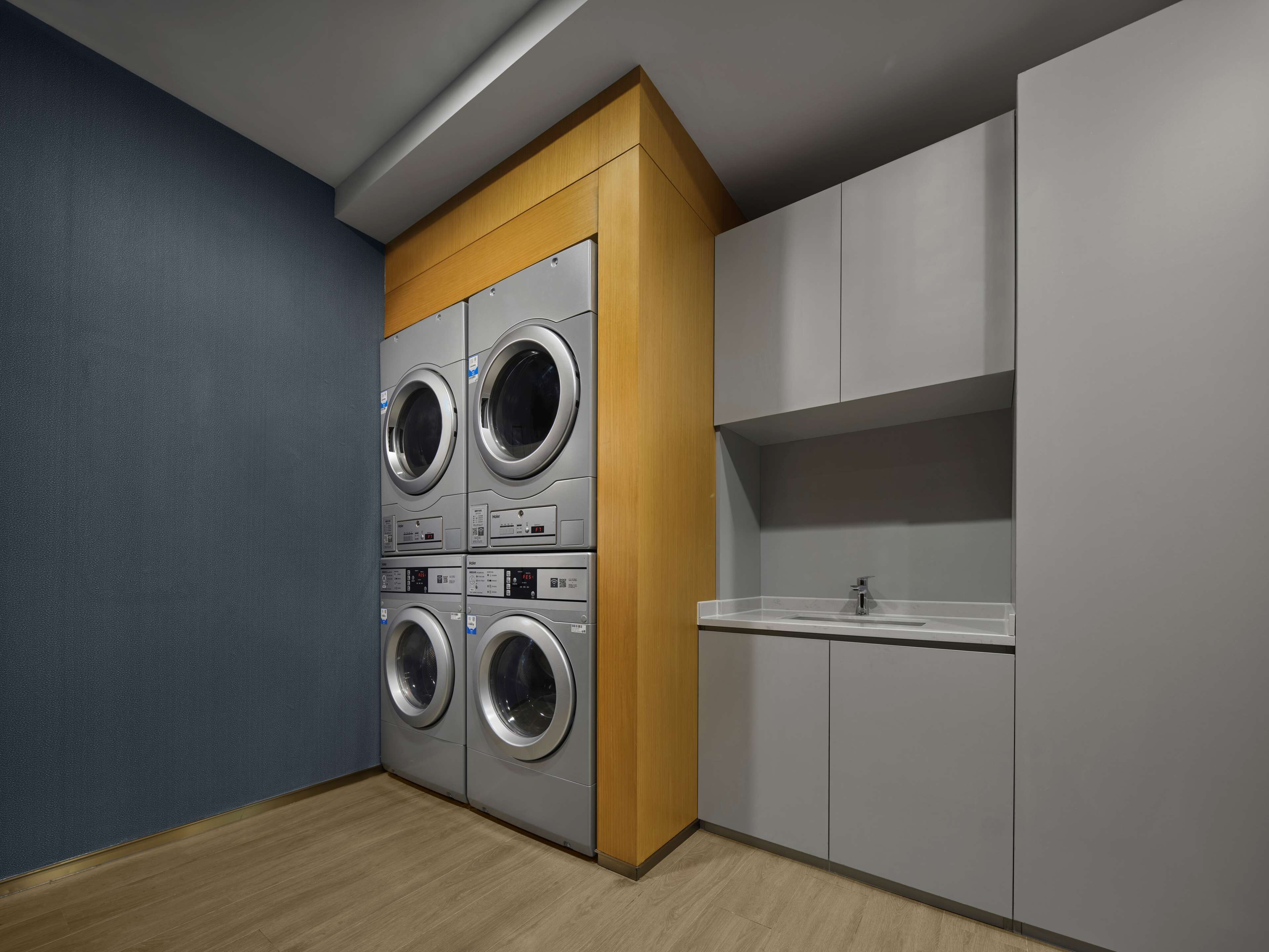 A laundry room with four stacked front-loading washing machines, a sink, and wooden cabinetry.