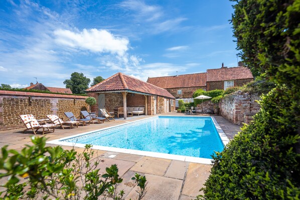 Une piscine avec des chaises longues, un espace de repos couvert et des murs en pierre.