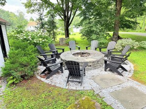 Un hogar circular de piedra rodeado por seis sillas Adirondack en un jardín.