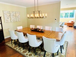 Un comedor con una mesa de madera, sillas blancas, una lámpara de araña y un tapete floral.