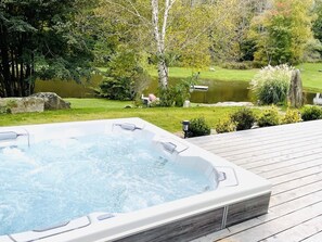 Un jacuzzi en una terraza de madera, con un estanque y árboles al fondo.