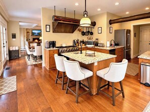 A modern kitchen with a central island, bar stools, stainless steel appliances, and a pendant light.