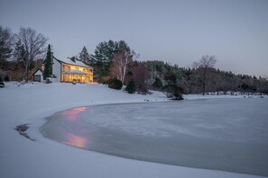 A snow-covered landscape with a house and a frozen lake. - The Manor - Modern Farmhouse with Hot Tub (West Dover)