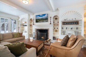 Una sala de estar con chimenea, un televisor sobre ella y una estantería con objetos decorativos.