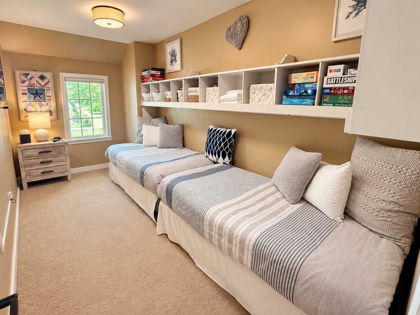 Une chambre à coucher comprenant un lit, des tables de chevet, une fenêtre et une étagère avec des livres et des objets décoratifs.