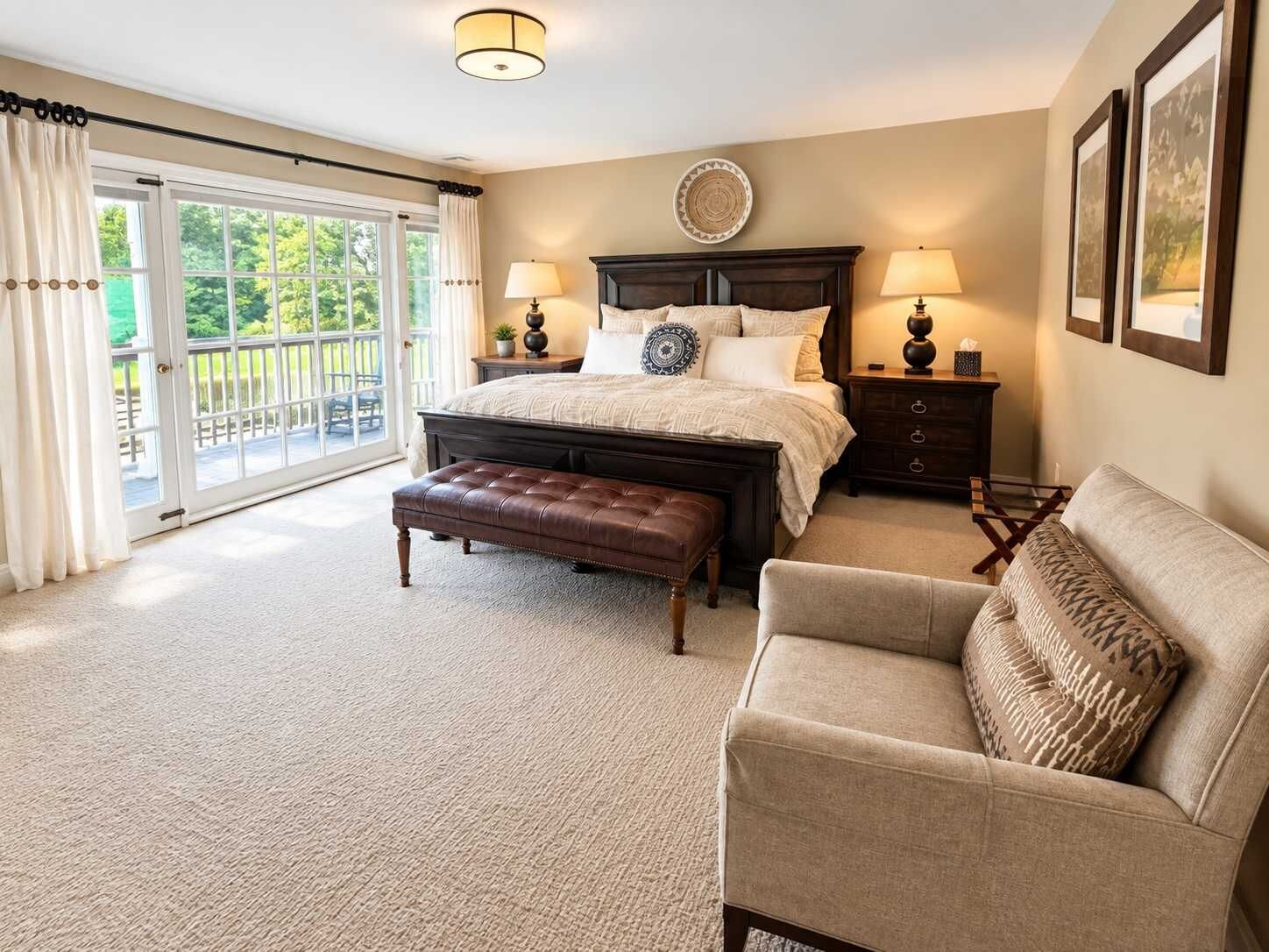 A bedroom with a large bed, a bench, a sofa, a nightstand, and a wall-mounted lamp.