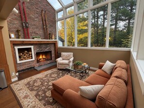 Una sala de estar acogedora con chimenea, un sofá y una ventana con vistas a árboles.