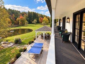 Un espacio al aire libre cubierto con mesa de ping pong, asientos y vista a un estanque y árboles.