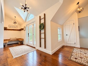 A spacious room with hardwood flooring, a wooden bench, a ladder, and a door with a wreath.