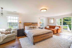 A bedroom with a wooden bed, a sofa, a chair, and a large window with a view of greenery.