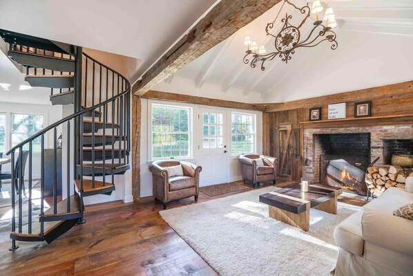 A spacious living room with a wooden staircase, a fireplace, and a chandelier.