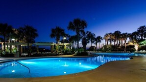 Une piscine au crépuscule, avec des palmiers et un espace abrité.