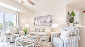 Un salon comprenant un canapé, des fauteuils, une table basse et un tableau représentant des voiliers.