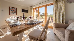 A dining area with a wooden table set for a meal, chairs, and a sofa. - Saltings House, Ringstead, Norfolk (Ringstead)