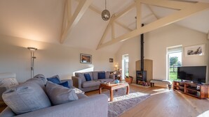 A spacious living room with a high ceiling, a fireplace, a television, and a sofa set. - Saltings House, Ringstead, Norfolk (Ringstead)