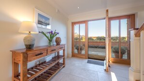 A wooden console table with a lamp and decorative items, a large sliding glass door leading to an outdoor area, and a framed picture on the wall. - Saltings House, Ringstead, Norfolk (Ringstead)