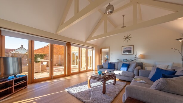 A spacious living room with a large TV, wooden flooring, a grey sofa, and a coffee table. - Saltings House, Ringstead, Norfolk (Ringstead)