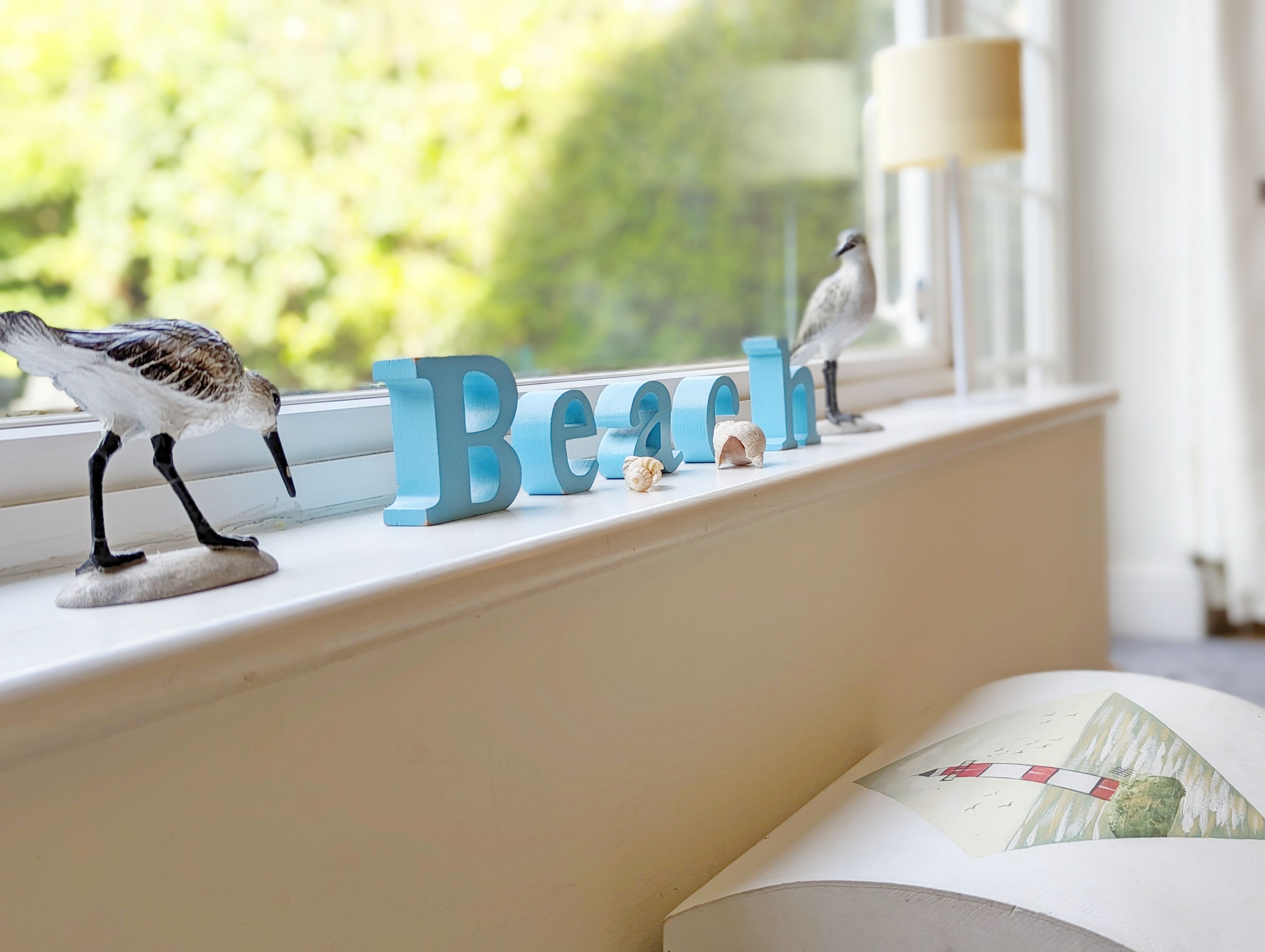 A window sill with decorative bird figurines, a nameplate spelling "Beach," and a small seashell.
