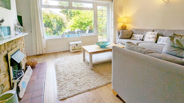 A living room with a fireplace, a sofa, a coffee table, and a view of greenery outside.