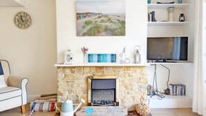 A living room with a stone fireplace, a painting of a beach, a clock, and a television on a shelf.