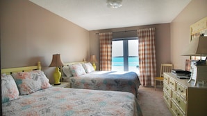 A hotel room with two beds, a dresser, a chair, and a view of the sea through the window. - CAPTAIN'S SUITE  Sea Coast (New Smyrna Beach)
