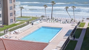 A pool area with a view of the ocean, surrounded by lounge chairs and palm trees. - CAPTAIN'S SUITE  Sea Coast (New Smyrna Beach)
