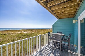 Eine Holzterrasse mit Tisch und Stühlen mit Blick auf einen Strand und Dünen.