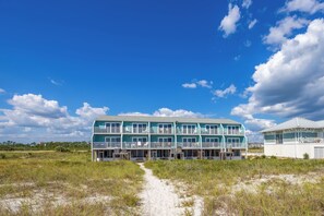Un edificio frente a la playa con varios balcones y un sendero de arena que lo conduce.
