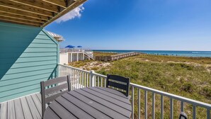 Une terrasse en bois avec une table et des chaises, donnant sur une plage avec une promenade en bois et des parasols de plage.