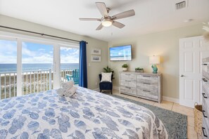 Un dormitorio con cama, ventilador de techo, televisor, cómoda, silla y vista al océano.