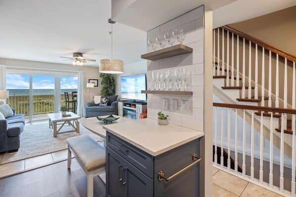Una cocina moderna con una isla central, estanterías empotradas para vinos y una escalera con barandillas de madera.