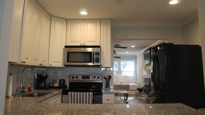 A modern kitchen with white cabinets, a stainless steel microwave, a black refrigerator, and granite countertops. - The Oasis in Murray Hill - Centrally Located- sleeps 8-  WiFi-Cozy-Free Parking (Jacksonville)