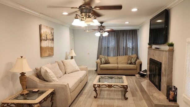 A living room with a beige sofa, a glass coffee table, a fireplace, and a ceiling fan. - The Oasis in Murray Hill - Centrally Located- sleeps 8-  WiFi-Cozy-Free Parking (Jacksonville)