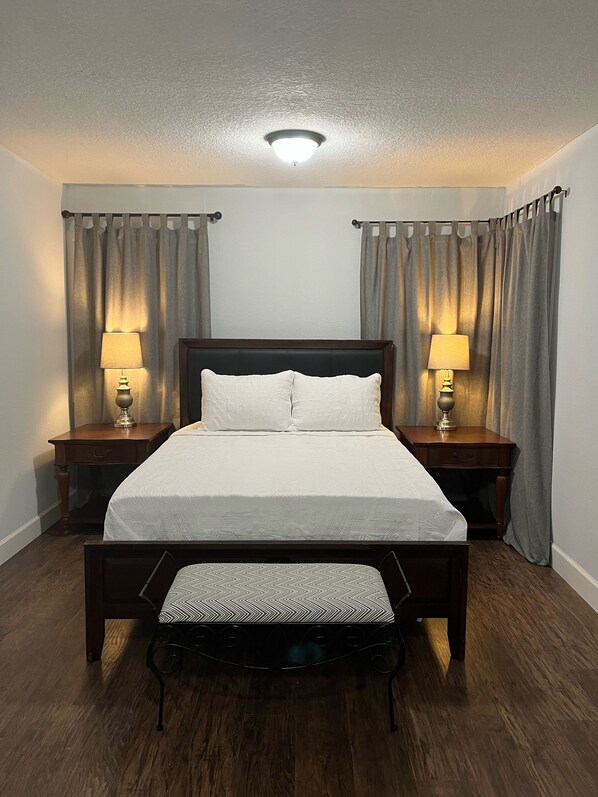 A neatly made bed with a wooden headboard, two bedside tables with lamps, and a bench at the foot of the bed. - The Oasis in Murray Hill - Centrally Located- sleeps 8-  WiFi-Cozy-Free Parking (Jacksonville)
