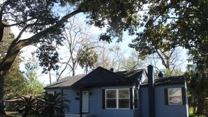 A single-story house with a dark blue exterior, a front porch, and a driveway. - The Oasis in Murray Hill - Centrally Located- sleeps 8-  WiFi-Cozy-Free Parking (Jacksonville)