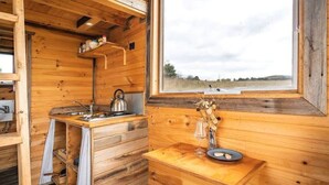 Ein Holzblockhaus-Interieur mit Küchenzeile, einem Fenster mit Blick ins Freie und einem Regal mit Küchenutensilien.