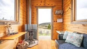 Ein gemütliches Blockhaus mit Kamin, Holzwänden, einer Couch und Blick ins Freie.