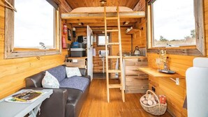 Ein gemütliches Blockhaus-Interieur mit Holzausstattung, einer Couch, einem Tisch mit einer Zeitschrift, einer Leiter und einer Küchenzeile mit einem Wasserkocher.