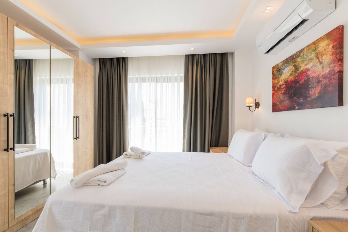 A hotel room with a large bed, a wardrobe, a painting on the wall, and an air conditioning unit.