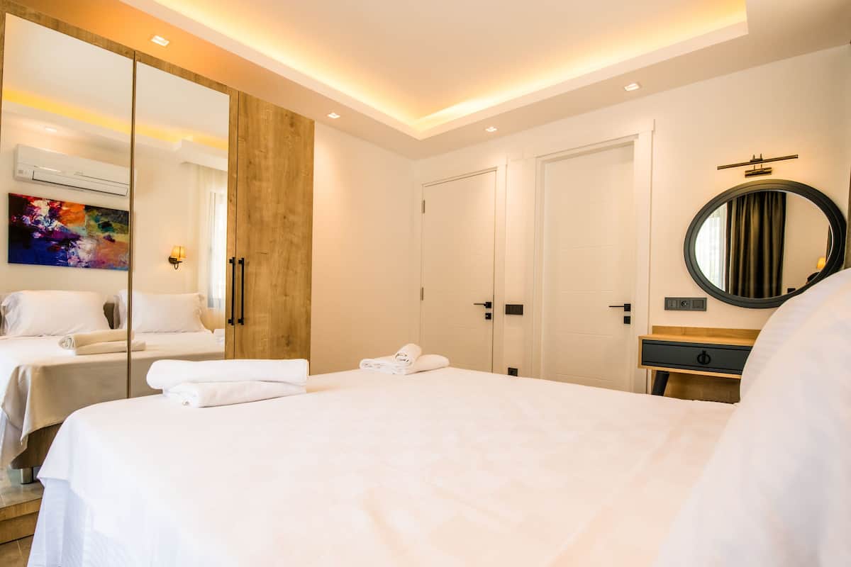 A hotel room with a large bed, a wardrobe with a mirror, a bedside table, and a wall-mounted round mirror.