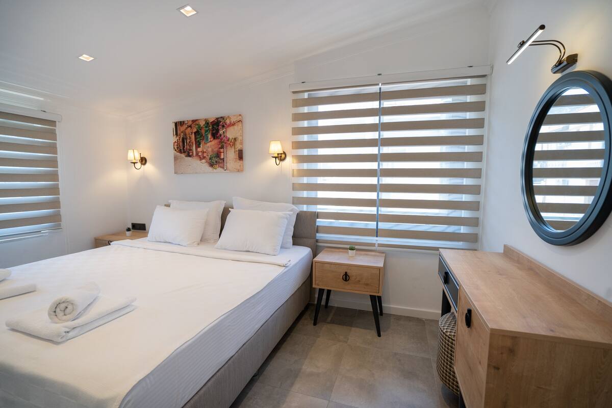 A modern bedroom with a large bed, bedside tables, a wooden dresser, and a round mirror.