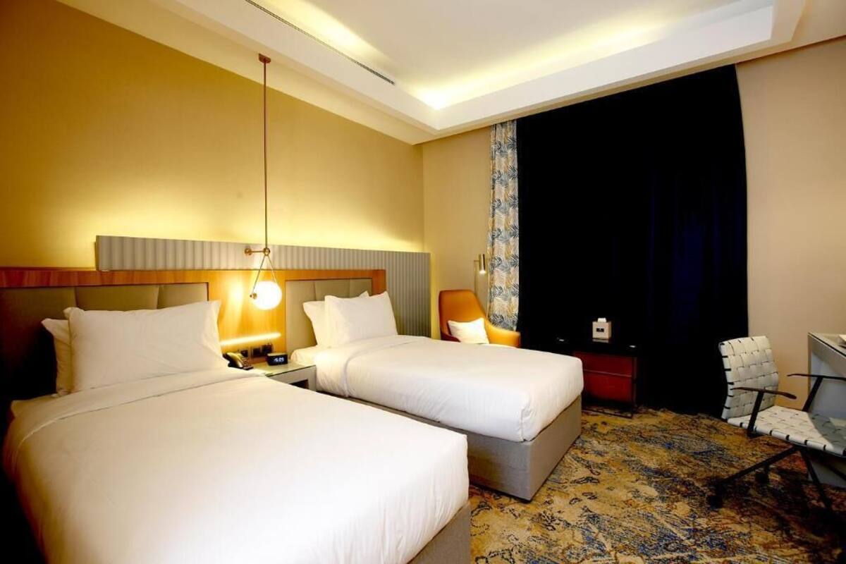 A hotel room with two beds, a desk, a chair, and a large window with curtains.