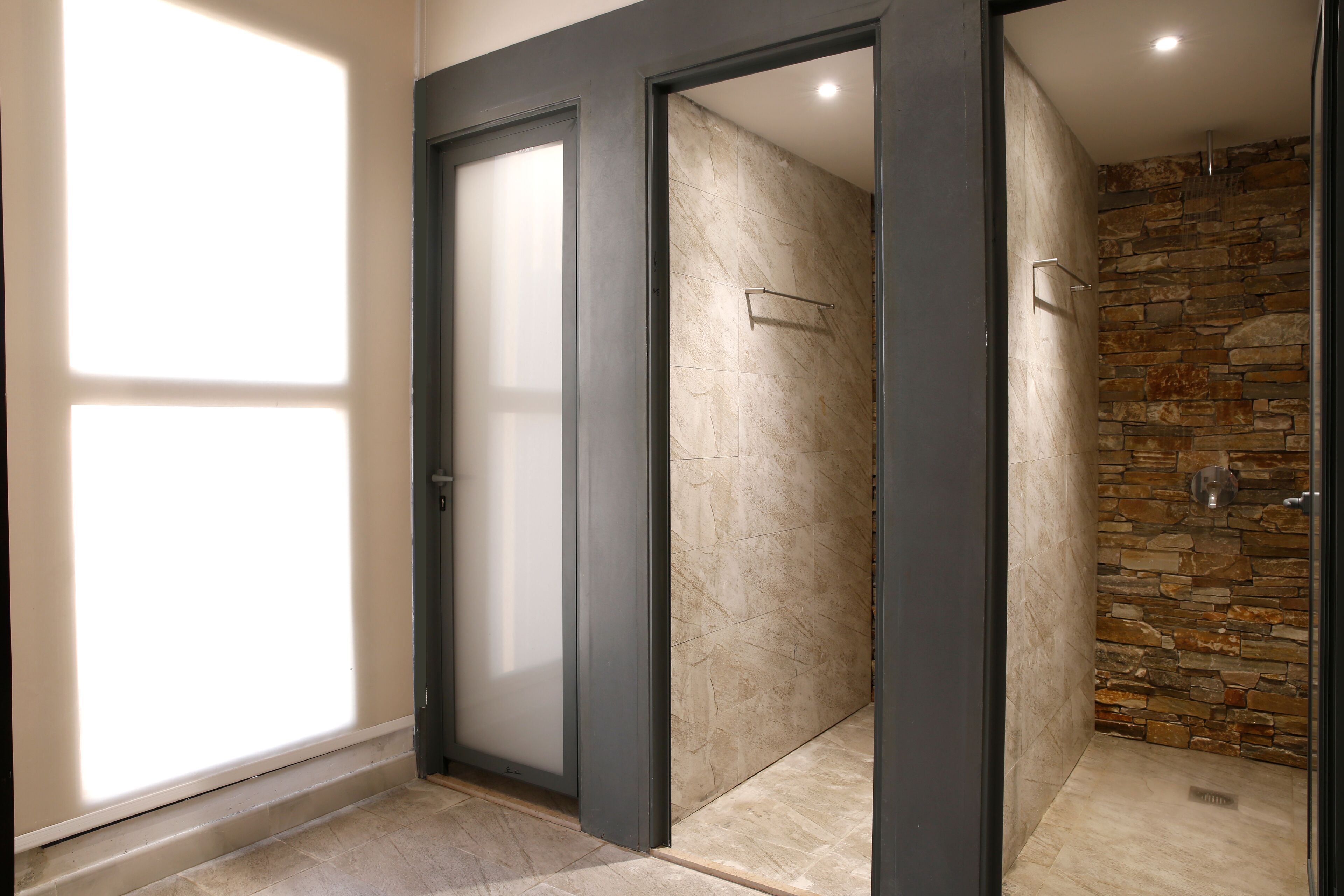 Un baño moderno con puerta de cristal, ducha con pared de piedra y suelo de baldosas.