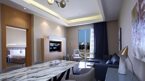 Una habitación de hotel moderna con una mesa de comedor de mármol, asientos cómodos, un televisor de pantalla plana y un balcón con vistas a la ciudad.